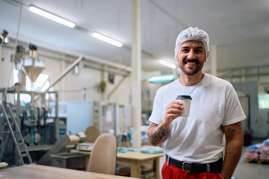 Manufacturing worker holding a coffee cup in a bright production facility.